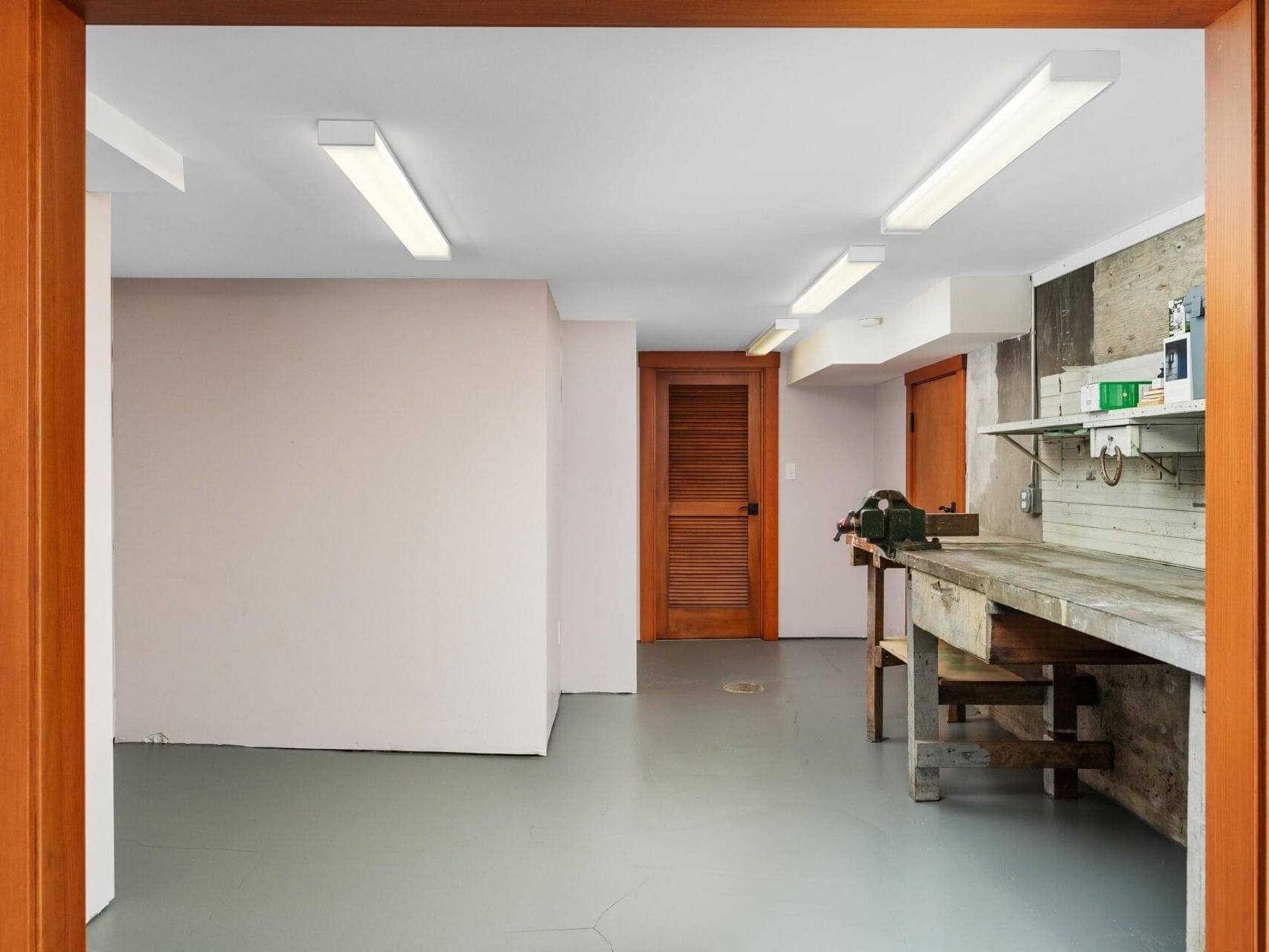 A clean, empty room in Portland, Oregon, boasts a concrete floor and fluorescent ceiling lights. It features a wooden workbench against one wall and a wooden door. The white-painted walls frame a wooden-framed doorway leading into the inviting space.