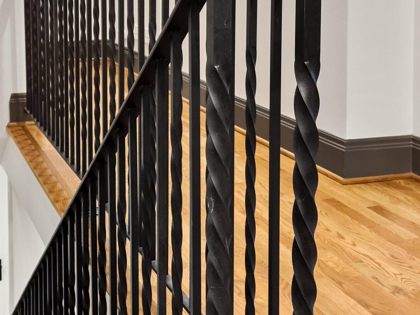 A black metal railing with twisted bars on a wooden staircase graces the home of a top real estate agent, set against white walls and a dark baseboard. The railing's design adds a decorative touch to the minimalist interior, emblematic of Portland Oregon real estate elegance.