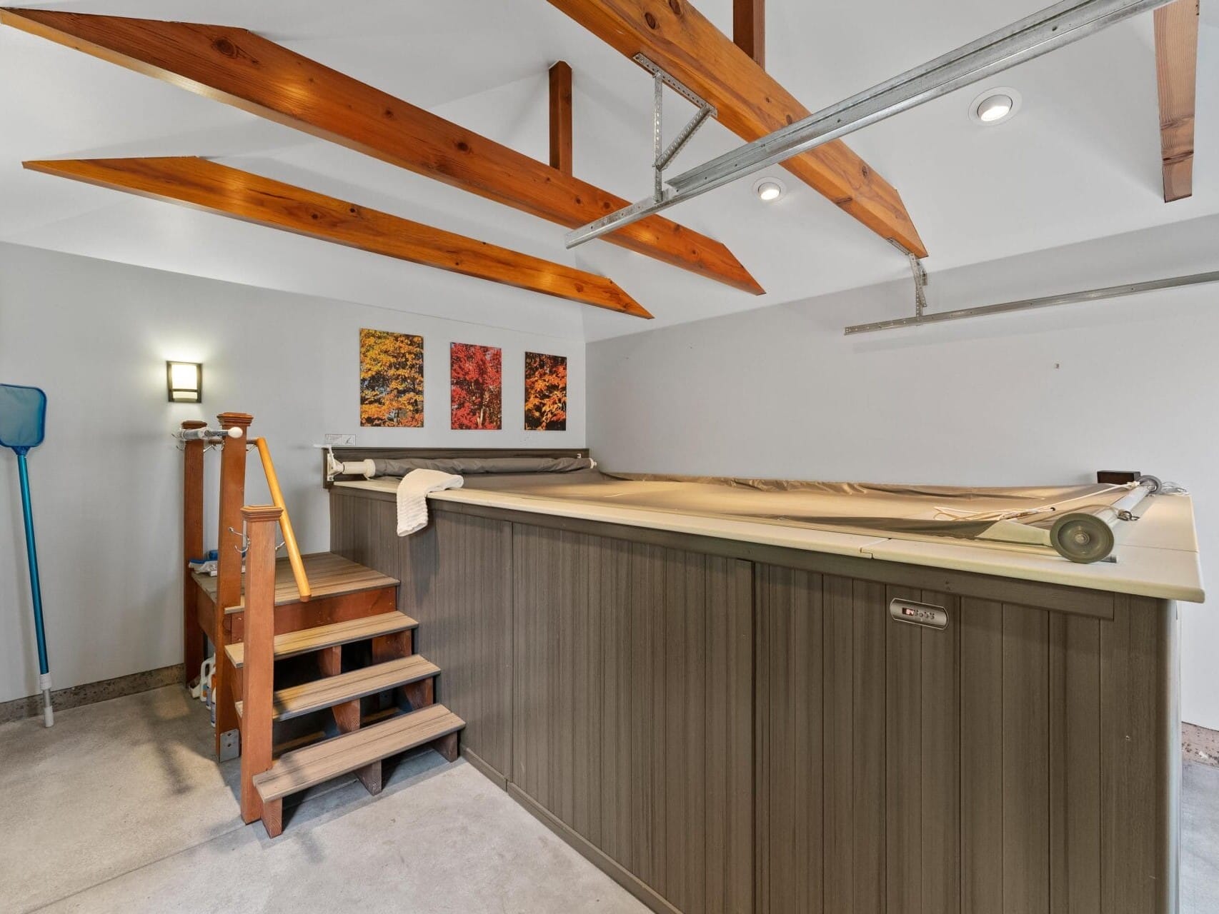 The interior of this Portland, Oregon room boasts a covered indoor pool with wooden steps leading up to it. The vaulted ceiling features exposed beams, while three colorful abstract art pieces adorn the wall. A pool net hangs on the left for convenience.