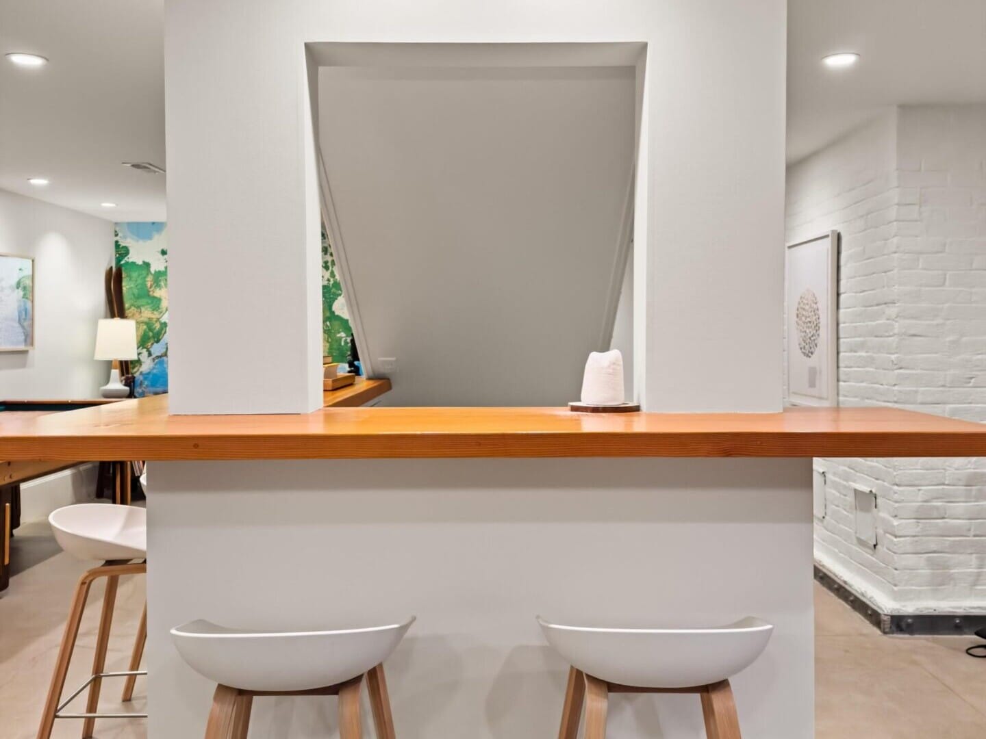 A modern kitchen nook with two white bar stools beneath a wooden counter sits in this Portland Oregon real estate gem. The area is well-lit, featuring recessed lighting on the ceiling. The space boasts clean, minimalist design with light-colored flooring and walls, ideal for any top real estate listing.