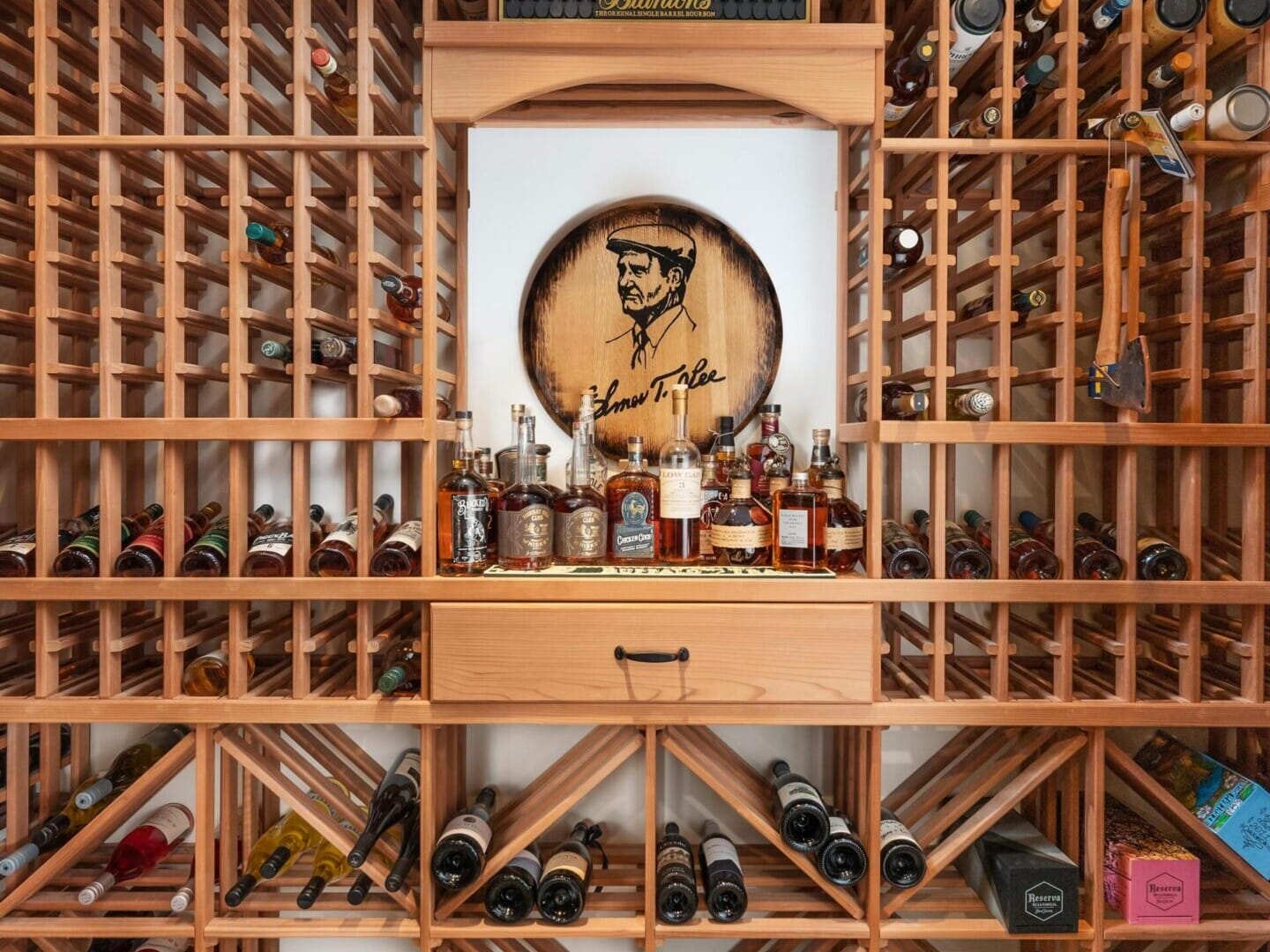 A well-organized wine cellar in a Portland Oregon real estate gem, featuring wooden racks filled with various wine bottles. A central display showcases several liquor bottles and a round wooden plaque with an illustration of a man. Soft lighting enhances the elegant setup, perfect for any top real estate agent to showcase.