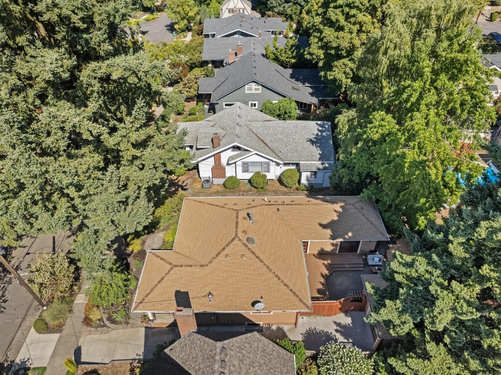 Aerial view of a suburban neighborhood in Portland, Oregon, with houses surrounded by trees. The scene shows a mix of different roof styles, a driveway, and lush greenery, providing a picturesque and peaceful residential area.