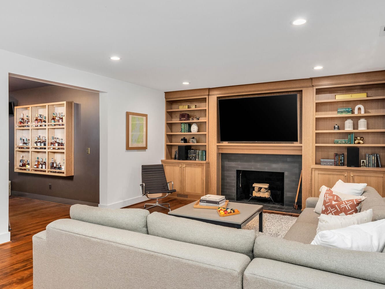 A modern Portland, Oregon living room features a gray sectional sofa, a wooden coffee table, and built-in shelves around the fireplace. The large flat-screen TV mounted above the fireplace complements the recessed lighting and cozy, contemporary design.