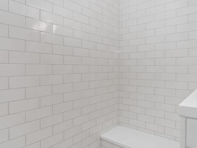 A shower area in Portland, Oregon, featuring white subway tiles on the walls and a small built-in bench. The floor is adorned with white hexagonal tiles subtly veined in gray. The scene is well-lit, highlighting a clean and minimalistic design.