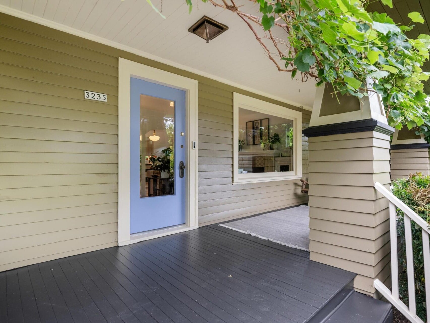 A cozy front porch with a light blue door and a large window sets the tone for this charming Portland Oregon real estate gem. Greenery climbs up a column, complementing the neatly painted black floor. The house number 3235 is prominently displayed, awaiting its next owner facilitated by a top real estate agent.