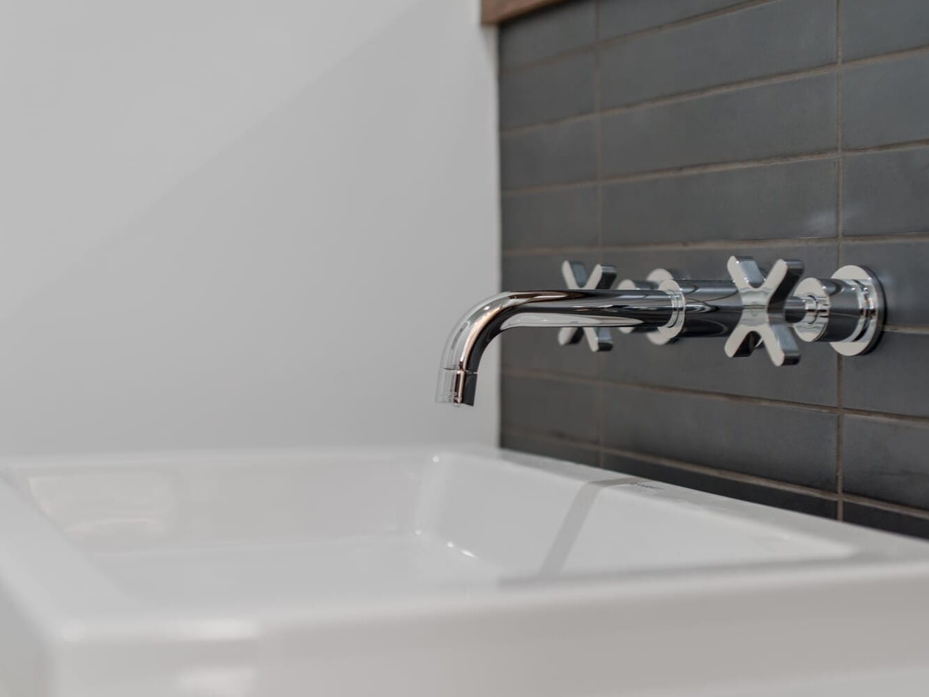 A modern bathroom sink with a sleek, chrome wall-mounted faucet above echoes the contemporary style found in Portland, Oregon. The set features two cross-handle taps on a gray tiled backsplash, while the white sink's clean, minimalist lines complete the design.