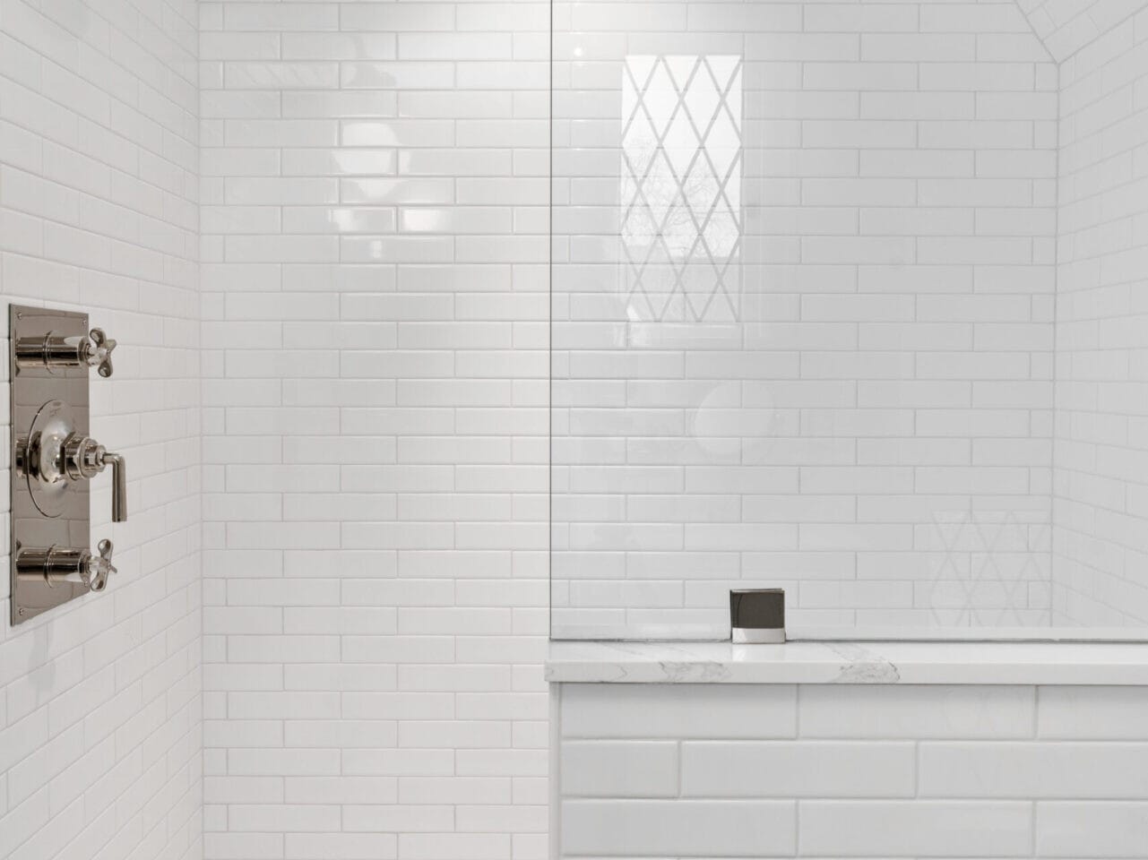 Minimalist white tiled shower with glass partition, reminiscent of sleek Portland, Oregon designs. Two chrome showerheads are mounted on the left, and the floor features a herringbone pattern. A frosted window on the right wall allows natural light to grace the space.